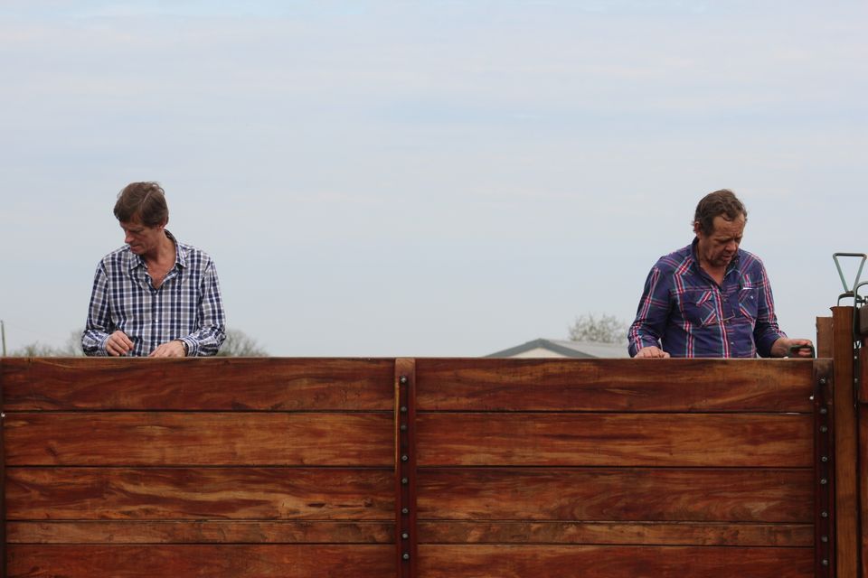 Stock view of two people working on a tall wooden fence